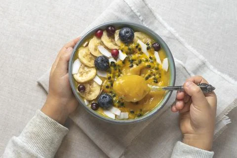 The child eats fruit puree.Children's hands hold a spoon and a bowl of smoothies Stock Photos