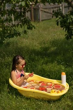 A child eats grapefruit while taking an outdoor bath filled Stock Photos
