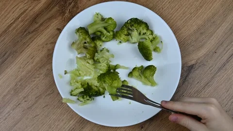 A child eats healthy food with a fork - vegetables, broccoli. White plate on Stock Footage 263439206
