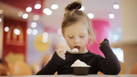 The child eats ice cream in a cup while sitting in a cafe. Close-up. The backgro Stock Footage 101054571
