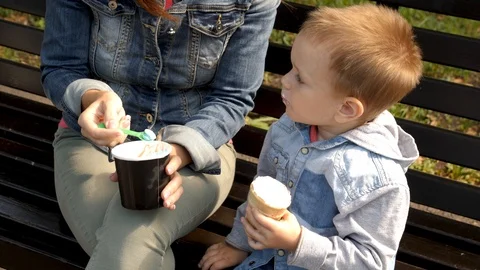 The child eats ice cream sitting on a bench. Young woman and child are eating 스톡 동영상 94051366