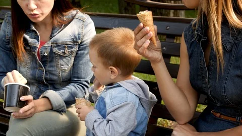 The child eats ice cream sitting on a bench. Young woman and child are eating Stock-Footage 94051597