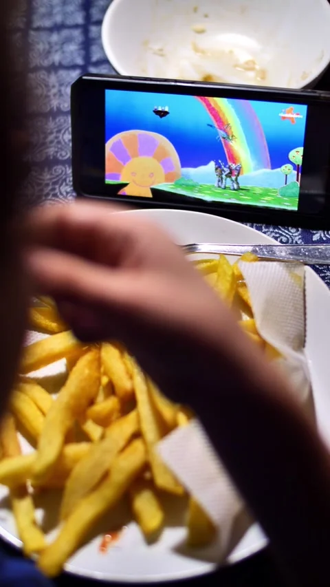 Child eats junk food and watches cartoons on the phone Stock Footage 258497202