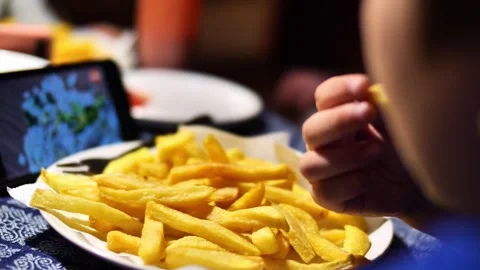 Child eats junk food and watches cartoons on the phone Stock Footage 258497602
