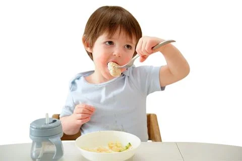 Child eats lunch with fork sitting at table on white background. Toddler boy  Stock Photos