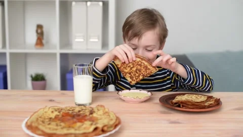 The child eats pancakes, dips them in condensed milk, he is happy. Stock Footage 194566069