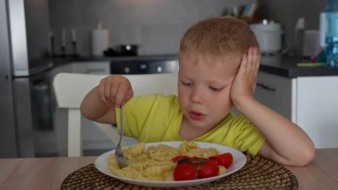 Child eats pasta shells and tomatoes for lunch in the kitchen. Stock Footage 290979103