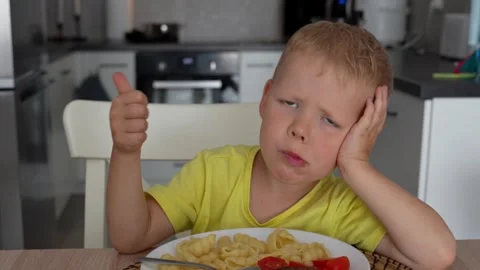 Child eats pasta shells and tomatoes for lunch in the kitchen in slow motion. Stock Footage 290979177