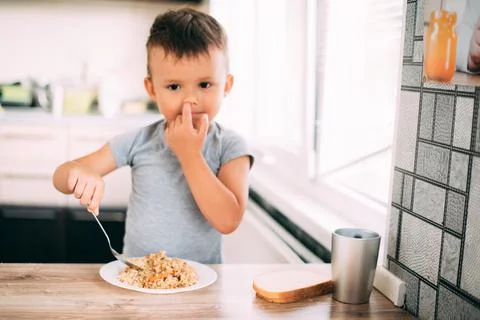 The child eats pilaf with carrots in the kitchen during the day Stock Photos