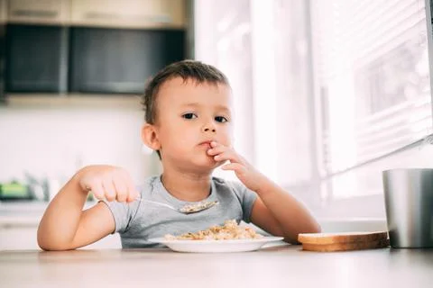 The child eats pilaf with carrots in the kitchen during the day Stock Photos