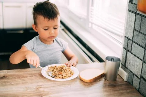 The child eats pilaf with carrots in the kitchen during the day Stock Photos