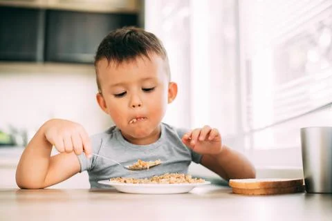 The child eats pilaf with carrots in the kitchen during the day Stock Photos