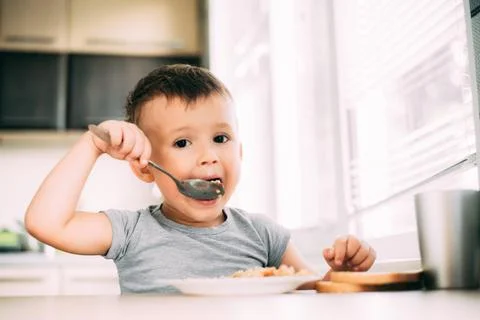 The child eats pilaf with carrots in the kitchen during the day Stock Photos