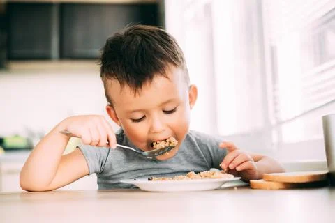 The child eats pilaf with carrots in the kitchen during the day Foto stock