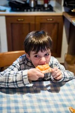 Child eats pizza sitting at the kitchen table Stock Photos