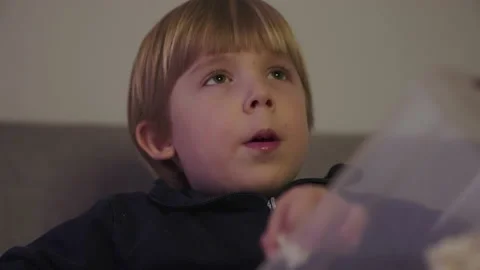 A child eats popcorn while watching tv Stock Footage 146313338