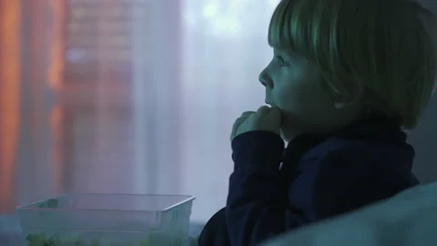A child eats popcorn while watching tv Stock Footage 146313339