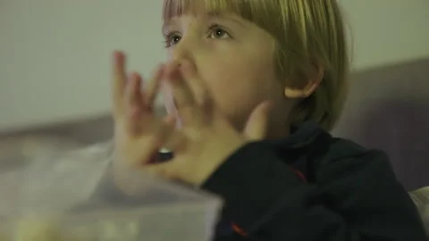 A child eats popcorn while watching tv Stock Footage 146313403