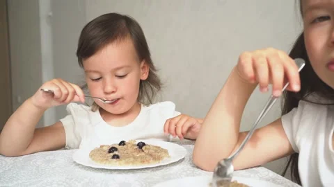 The child eats porridge with berries. The two sisters eat breakfast and Video stock 157635900