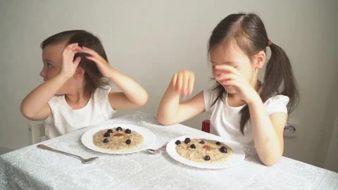 The child eats porridge with berries. The two sisters eat breakfast and Video stock 157747042