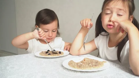 The child eats porridge with berries. The two sisters eat breakfast and Video stock 157799003