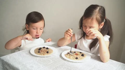 The child eats porridge with berries. The two sisters eat breakfast and Video stock 157953347