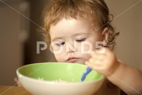 Child eats porridge. Portrait of serious male kid eating Stock Photos