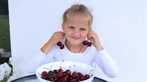 The child eats ripe cherries with appetite and plays with them. The girl eats a Stock Footage 194671787