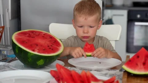 Child eats a slice of watermelon at the kitchen table in the kitchen at home. Stock Footage 290983889