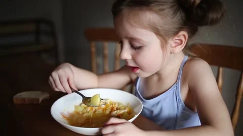 Child eats soup with spoon from plate at home in kitchen at table. 動画素材 147729337