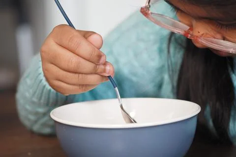 Child eats with a spoon from a blue bowl at home Stock Photos