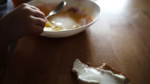 Child eats with spoon from plate at home in kitchen at table. 動画素材 147729348