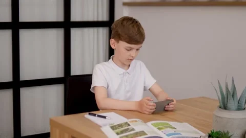 A Child Engaged with a Smartphone While Sitting at a Study Table is Focusing on Stock Footage 312195797