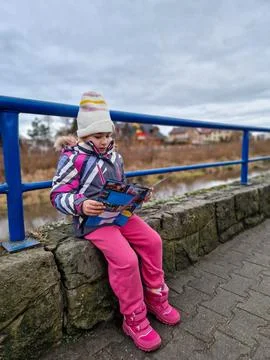 A Child Engaging in Reading While Dressed in Warm Winter Attire in the Grea.. Stock Photos