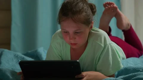Child engrossed in screen, relaxed on bed with legs up Stockbeeldmateriaal 333513727