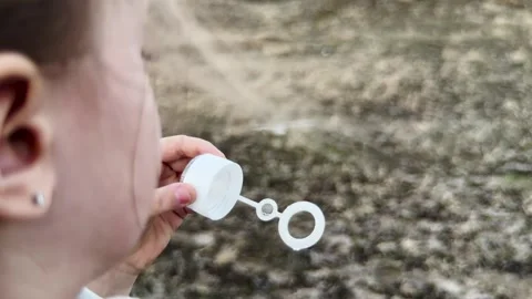 Child enjoying blowing bubbles in open space, soft glow of the sunset, nature s Stock Footage 316709603