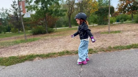 Child enjoying roller skating on a green park pathway Stock Footage 345634025