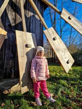 A child enjoying the winter sun by a rustic wooden windmill Stock Photos