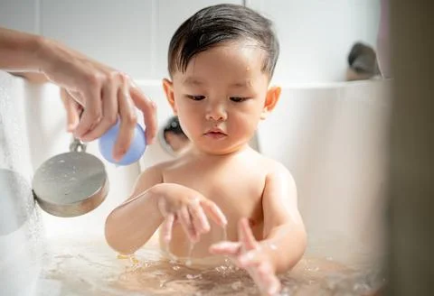 Child enjoys bath time while playing with water in a cozy bathroom setting .. Stock Photos