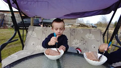 Child enjoys ice cream while sitting outside on a swing in a backyard setting du Video stock 332064895