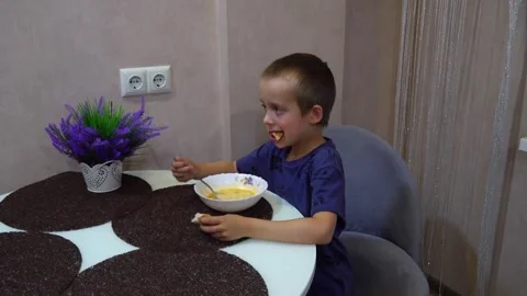 Child enjoys snack at home while sitting at a table in a cozy room with flowers Stock Footage 340448051