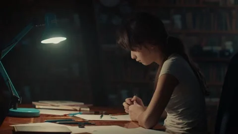Child enthusiastically draws while sitting at table under light of table lamp Stock Footage 145543712