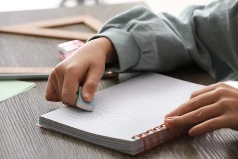 Child erasing mistake in notebook at table, closeup Foto stock