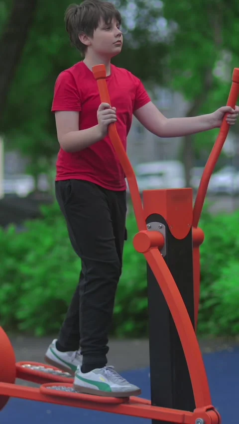 Child Exercising on Outdoor Elliptical Machine in Park, Healthy Stockbeeldmateriaal 338013747