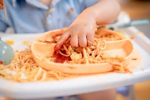 Child explores meal with hands while sitting in high chair during mealtime .. Stock Photos