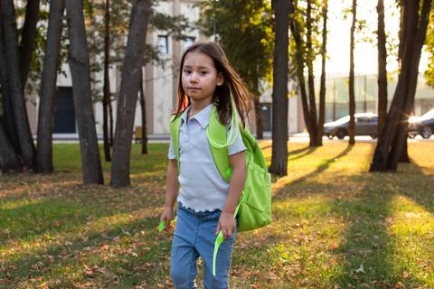 Child exploring park with green backpack during golden hour Stock Photos