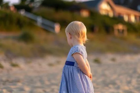 Child exploring the sandy beach at sunset while wearing a striped dress and Stock Photos