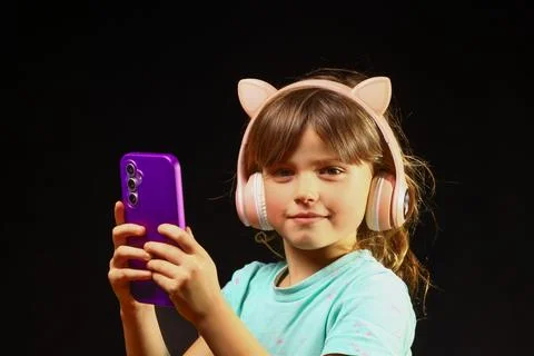 Child exploring a smartphone with wireless cat‑ear headphones, Stock Photos