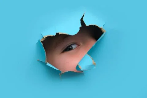 Child eye looking through a hole in blue paper. Curiosity and investigation.. Stock Photos