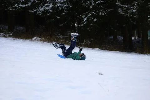 Child falling off a blue snow sled while sliding down a snowy hil Stock Photos